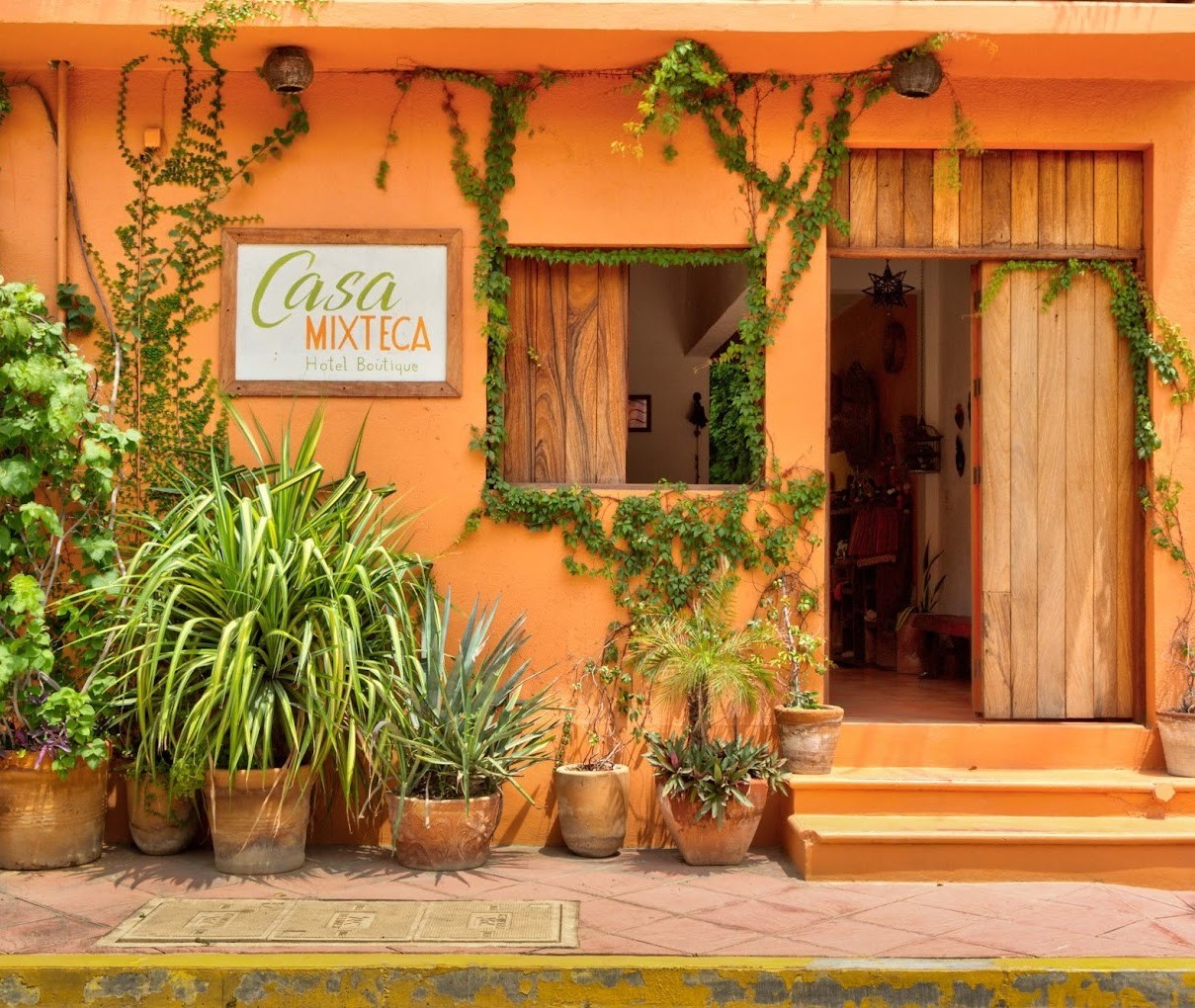 casa_mixteca vista del exterior del hotel Casa Mixteca con puerta de madera, fachada color naranja y macetas en Zipolite, Oaxaca