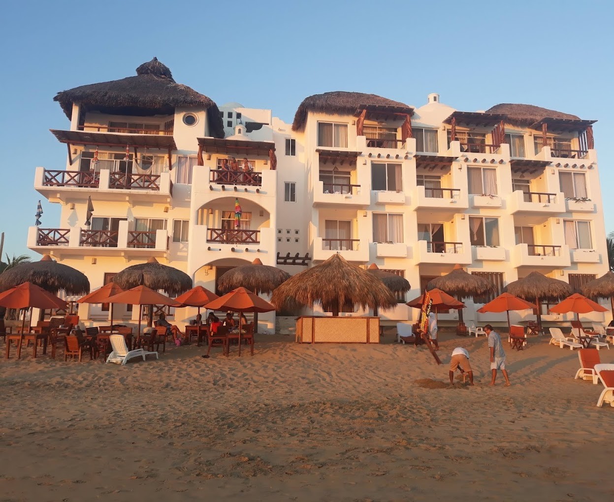 playa_zipolite_hotel vista del exterior de hotel playa Zipolite a pie de playa, edificio blanco con camastros y parasoles